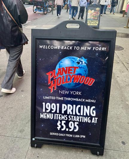 Sidewalk tent, advertising Planet Hollywood’s 1991 pricing. Legs of someone walking past.