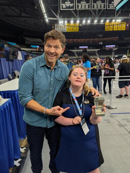 A young woman with Down syndrome cosplaying as a Starfleet officer standing next to Mischa Collins. He's smiling and pointing at her