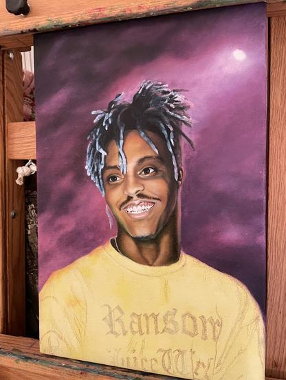 Oil painting in progress - portrait of Juice Wrld looking off to his right and smiling, wearing a yellow Ransom t-shit. His hair is still in the underpainting stage of monochromatic blue and I haven’t painted his beard yet. The background is a smoky purple and magenta with a spotlight shining down from the upper right. It’s reflecting off his neck, jaw, and hair on his left side.