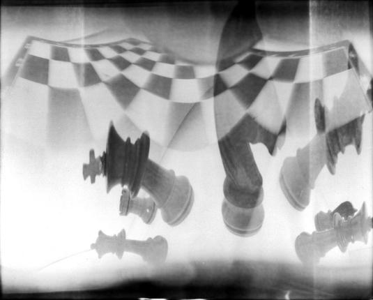 Ein räumlich verzerrtes Lochkamerafoto bildet als Doppelbelichtung Schachfiguren und ein Schachbrett ab.