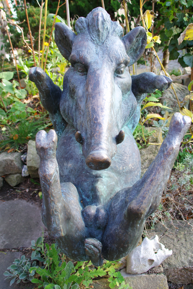 Eine Bronzefigur in Form eines auf dem Rücken liegenden Wildschweins, alle vier Beine von sich streckend.