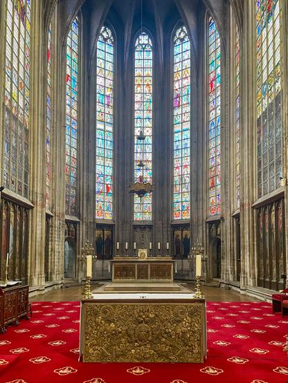 Interior view of the church with tall stained glass windows and golden altars, filling the space with colored light and quiet calm.