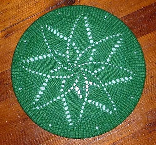 a top down photo of a lacy green tam, the lace pattern resembles a spiral flower.