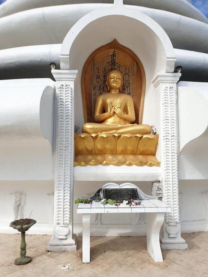 Bouddha doré assis sur une fleur de lotus, devant le mur blanc de la pagode de Rumassala au Sri Lanka.