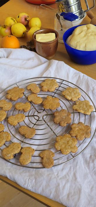 Haferflockenplätzen auf einem Abkühlgitter, das mit anderen Backzutaten auf einem Tisch aus hellem Birkenholz steht.