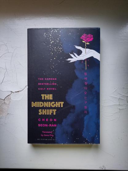 Kirjan tummassa kannessa näkyy sinistä savua sekä valkoinen piirretty käsi, jonka lävistää punaisen ruusun varsi.