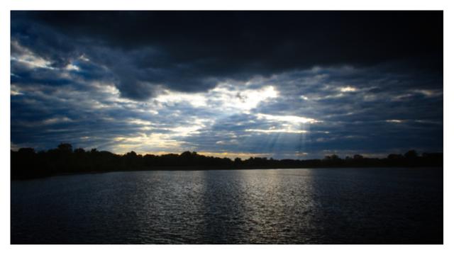 Dark sunset with overcast clouds with two pillars of light reflecting on the water.