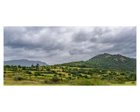 A panoramic view of rolling hills and rain clouds with a grassy meadow in the foreground.