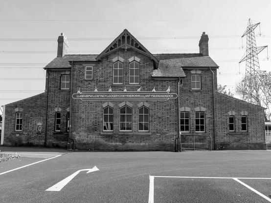A brick building seen from the front. On the façade is written "Llanfairpwllgwyngyllgogerychwyrndrobwllllantysiliogogogoch", the longest town name in Europe.