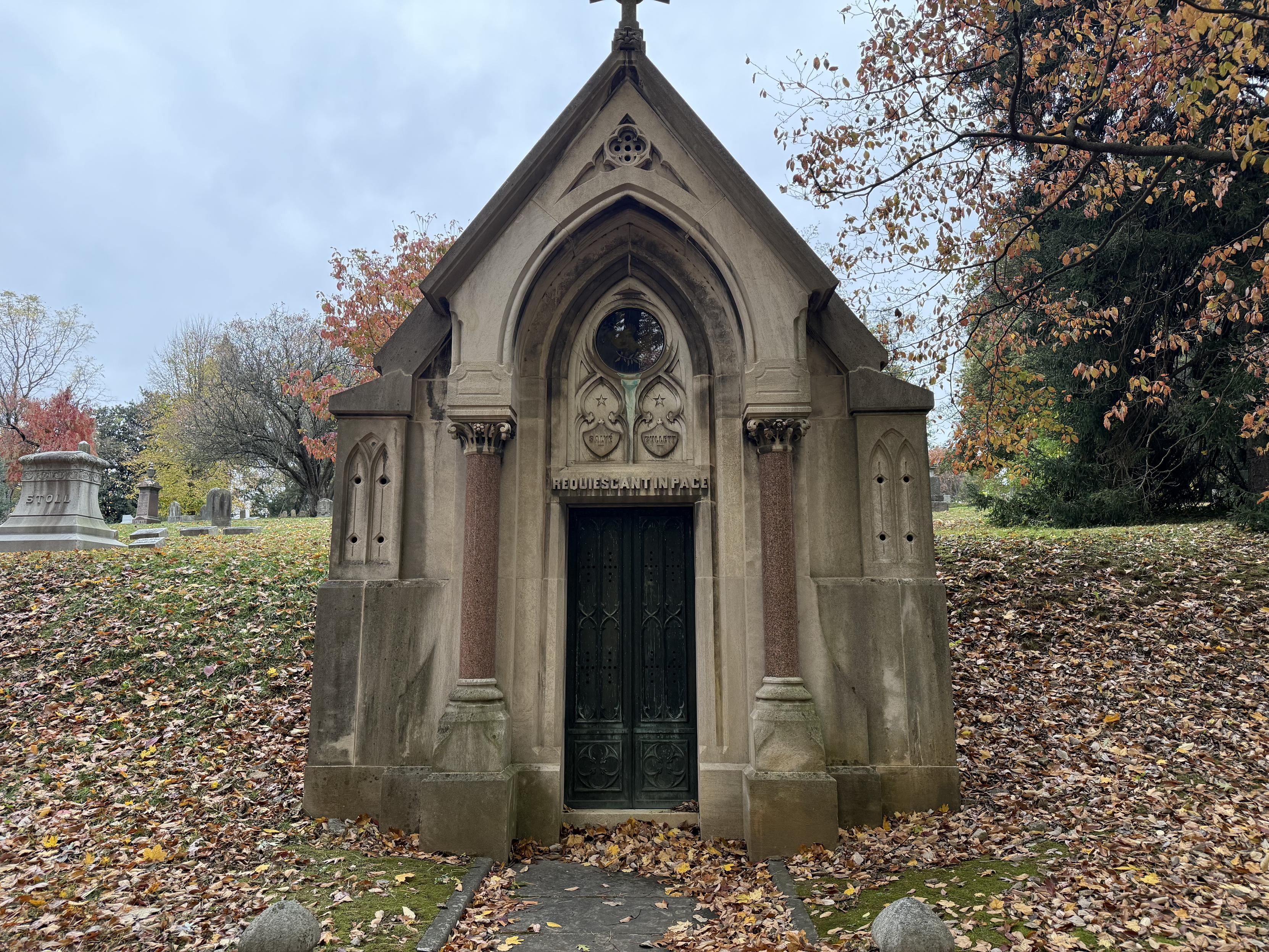 A cemetery crypt with an ornate entryway and steepled roof.