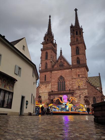 Foto. Strassenszene mit Kirchenfassade in Sandstein, davor ein Fahrgeschäft.