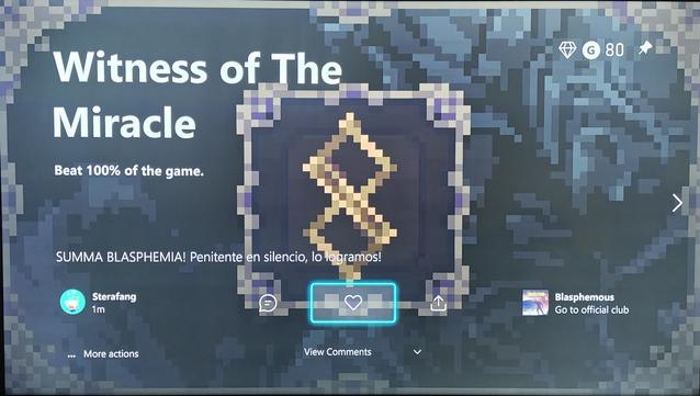 A photo of a TV showing an Xbox achievement post. The achievement is for the game Blasphemous and is titled "Witness of The Miracle", with 80 points. The description states: "Beat 100% of the game.", and the image shows the game's iconic twisted crucifix. 

Below the title, there is a comment from the uploader, Sterafang, in Spanish: "SUMMA BLASPEHMIA! Penitente en silencio, lo logramos!" ("Penitent one, we did it!")