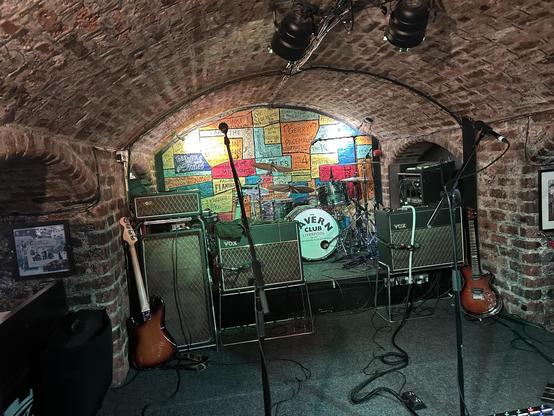 Empty stage with musical instruments and colorful posters on brick walls at The Cavern Club in Liverpool.