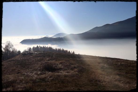 Paesaggio montano dove le vette emergono dalle nuvole basse. Un raggio di sole illumina una parte della foto