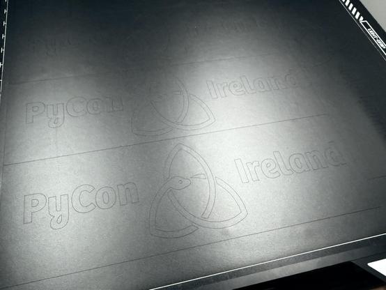 The image shows a black surface with the faintly engraved text "PyCon Ireland" and a logo design. The material is a matte black vinyl, fresh from the cutter.