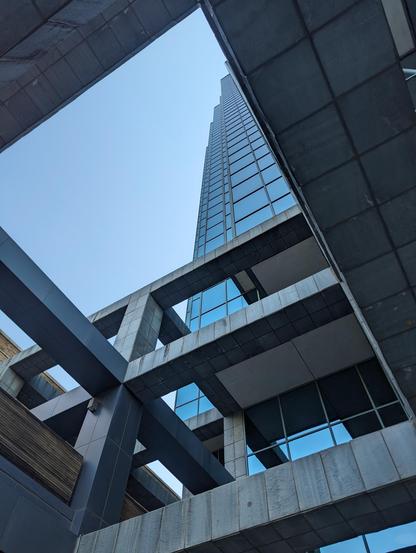 Looking up through the structure of the building at the corner of North St Paul St and Ross Ave in downtown Dallas, TX.

Square geometric latticework of concrete with some wood accents, framed vertically and offset at an angle, with the glass skyscraper part of the building partially visible through the latticework.