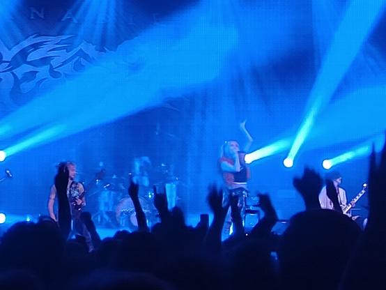 Hanabie on stage all lit up in blue. Audience with hands in the air in the foreground.