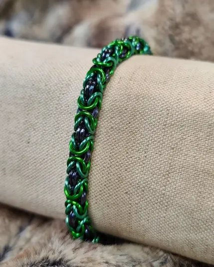 Bracelet en maille, composé majoritairement d'anneaux verts de deux tons différents. Montré ici sur un présentoir.