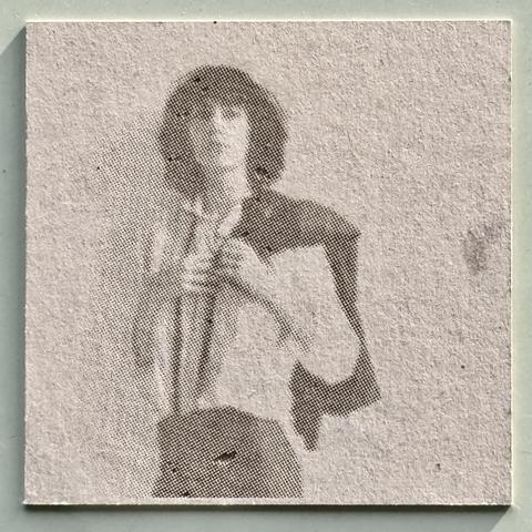 A woman in a white shirt and a jacket thrown over the shoulders looking into the camera. Her photo is printed on grey cardboard using a laser cutter.