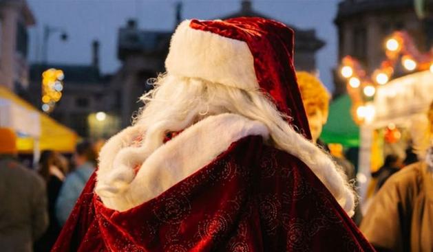 Traditional Santa walking through festive Christmas market with lights and stalls in Swansea.