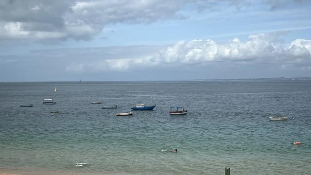 Un océano de mar transparente donde se ven barcazas y un cielo con nubes