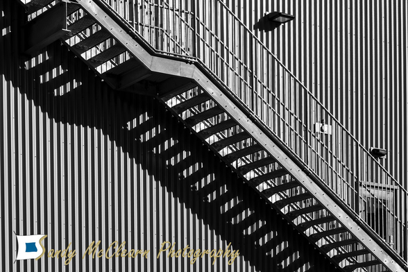 Metal stairs cast a shadow amidst the glare off a building’s metal siding.
