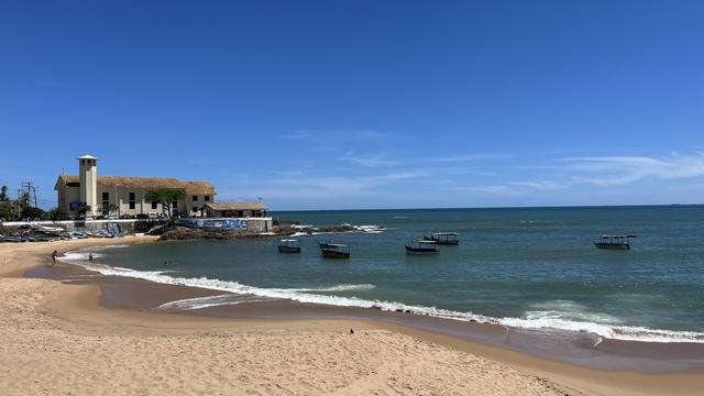 Un océano de mar transparente donde se ven barcazas y a la izquierda un faro