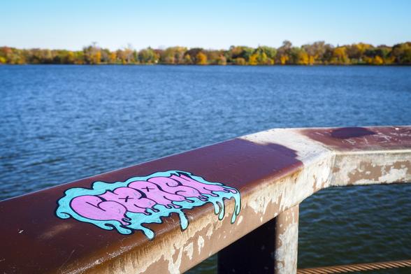 Blue and pink graffiti tag that says CRASH on a rusty metal platform overlooking a lake