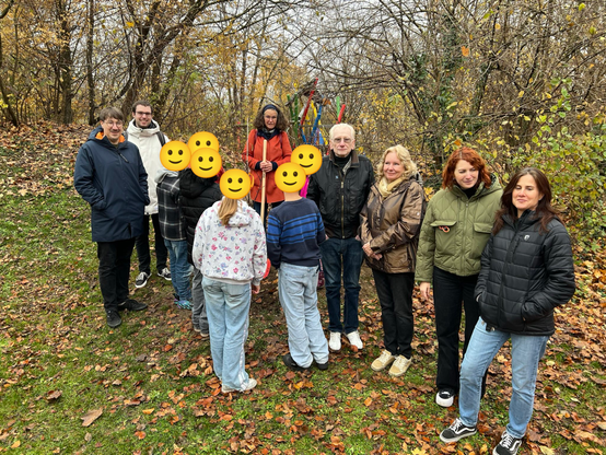 Gruppenfoto um einen frisch gepflanzten Baum. In der Mitte stehen sechs Kinder, deren Gesichter jeweils von einem Smiley verdeckt sind.