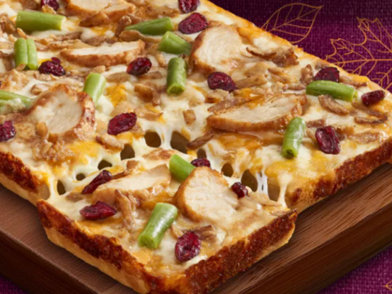 A square pizza is seen. Toppings include sliced turkey, green beans, cranberries, and cheese.