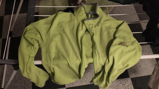 Eine lime-grüne Fleecejacke liegt flach auf einem Wäscheständer, unten drunter karierter Granitboden
