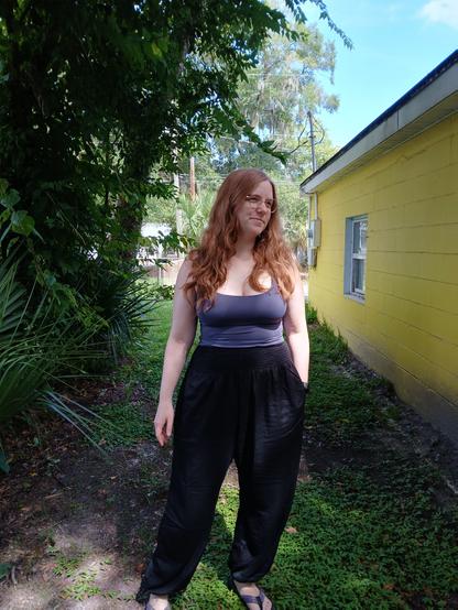A redheaded lady standing by a yellow house.