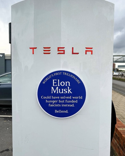 Tesla symbol with a big blue circular sticker saying ‘world’s first trillionaire Elon Musk could have solved world hunger but funded fascists instead.’