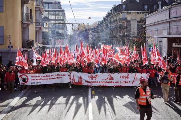 A large crowd marches down a street, carrying red and white flags