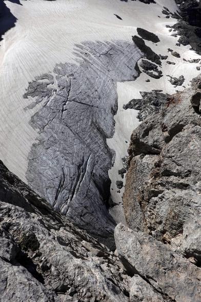 Ein zur Hälfte aperer und zerklüfteter Gletscher in felsigem Terrain dominiert das Bild.