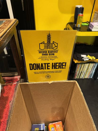 A sign stating „donate here“ above a cardboard box.