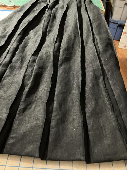 The detail of edge stitching holding the pleat lines secure from hip to hem is shown on the black linen skirt on a table