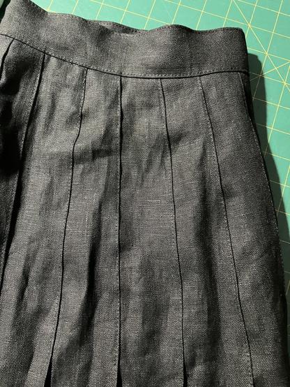 Waistband and pleated top stitched black linen skirt on a green cutting mat