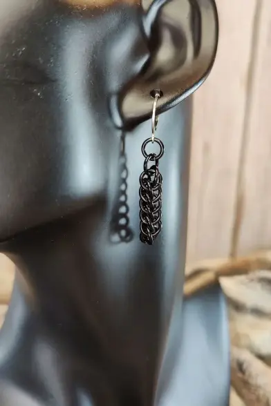 Boucle d'oreille en maille, composée d'anneaux en aluminium anodisé noir. Montrée ici attachée à l'oreille d'un présentoir adapté.
