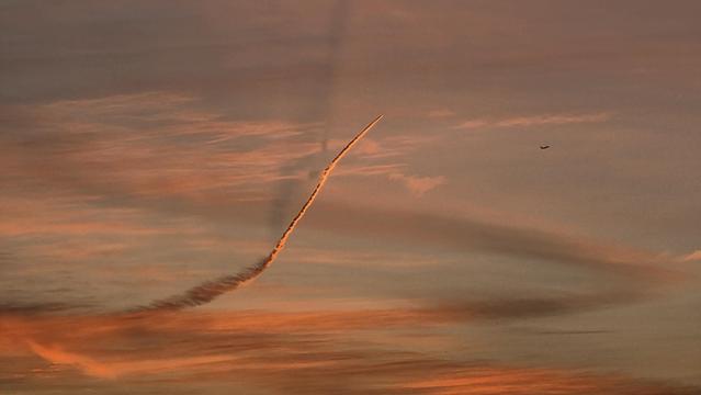 Kondensstreifen eines startenden Flugzeugs im Licht der aufgehenden Sonne