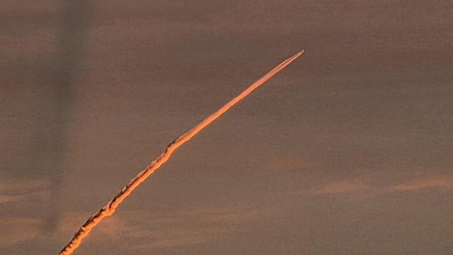 Kondensstreifen eines startenden Flugzeugs im Licht der aufgehenden Sonne