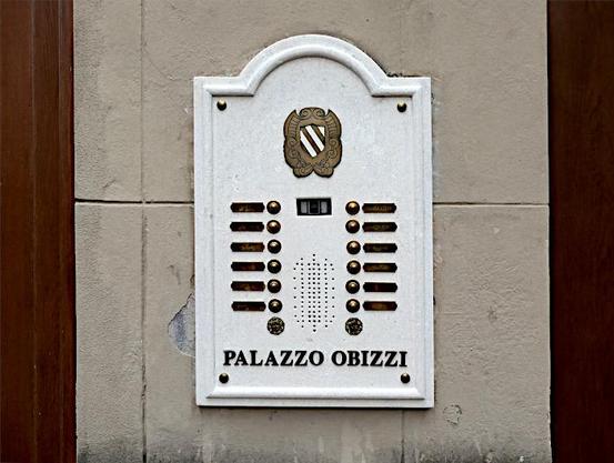 Foto van twee rijen deurbellen met naambordjes onder een wapen gevat in een stenen plaat