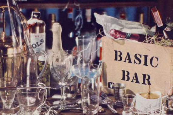 1958 Classic Bar Setup - Vintage Attraction

The image displays an assortment of barware and alcohol bottles arranged on a table, with the prominent text "BASIC BAR" printed on what appears to be a cardboard or paper box.
Various glass drink containers are visible alongside several types of spirits in bottles.