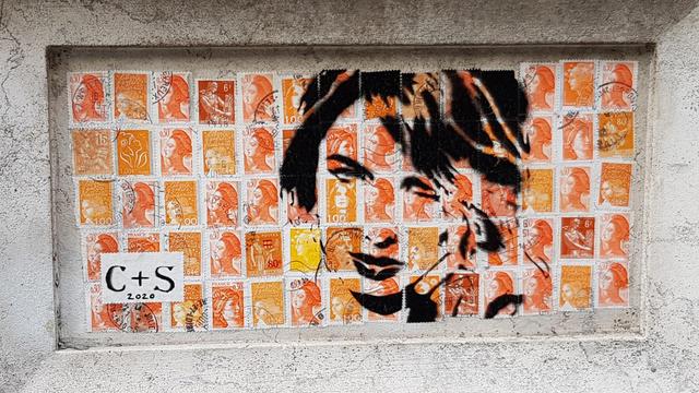 Drawing of a woman's face on orange French post stamps. Framed in a feature of a carved stone pillar.