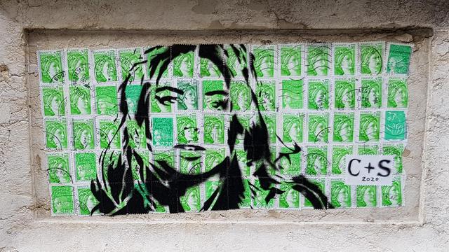 Drawing of a woman's face on green French post stamps. Framed in a feature of a carved stone pillar.