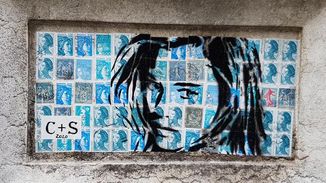 Drawing of a woman's face on blue French post stamps. Framed in a feature of a carved stone pillar.