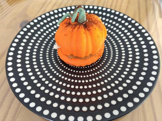 Pâtisserie en forme de citrouille sur une assiette noire à points blancs