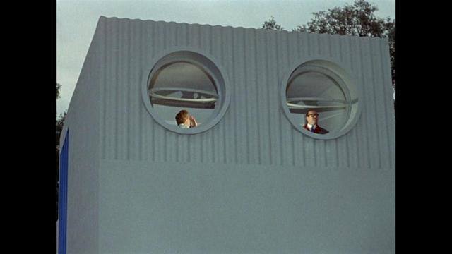 still from Mon Oncle, a modern house, Villa Arpel has two round windows. The couple that lives there each stand behind a window, the windows are opened.