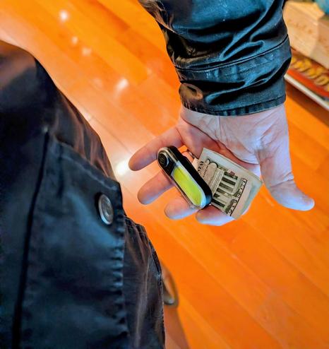 Downward-shot photo of my coat pocket, LED safety light and a $5 bill