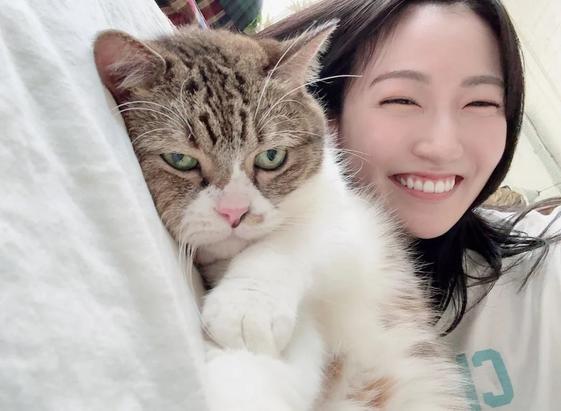 A woman smiling lying in a bed with her cat.